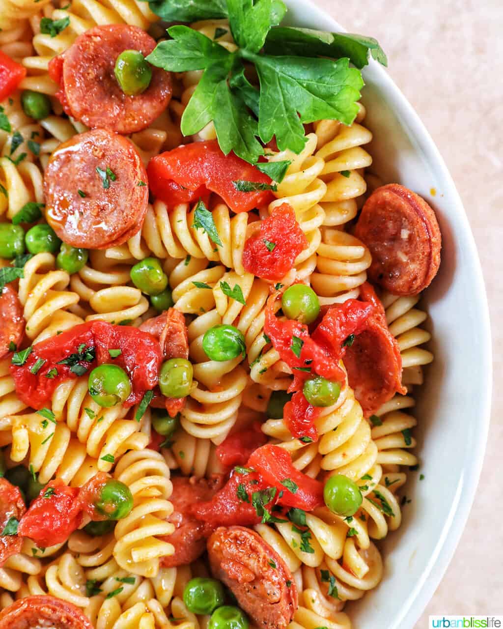 half a bowl of linguica pasta with tomatoes, herbs, peas, and linguica.