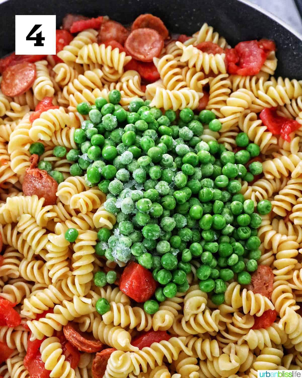 peas on top of pasta, tomatoes, and linguica in a skillet.