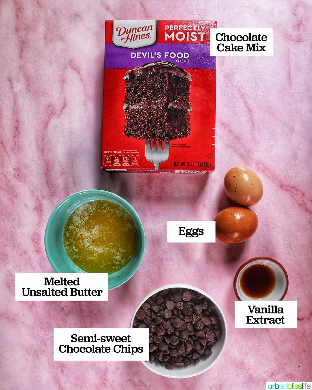 box of cake mix and bowls of other ingredients to make chocolate chip cake mix cookies on a pink table.