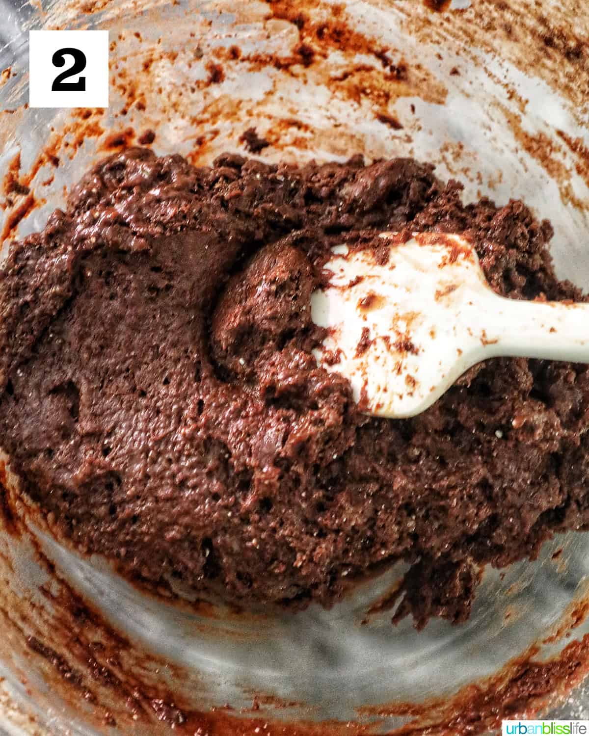 chocolate cake mix cookie batter with white spatula in a glass mixing bowl.