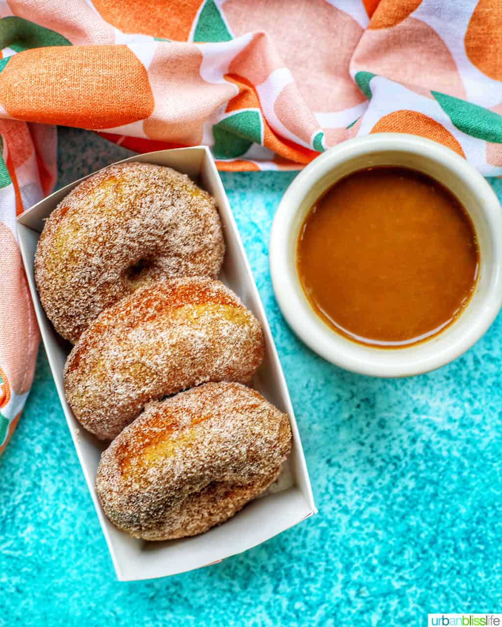 three apple cinnamon donuts in a box with cup of coffee