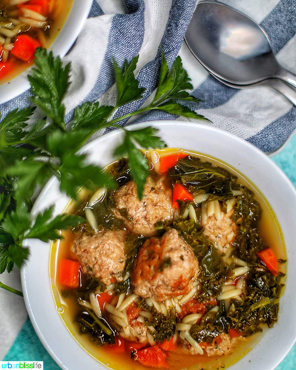 single white bowl of instant pot Italian Wedding Soup with two spoons and parsley garnish.