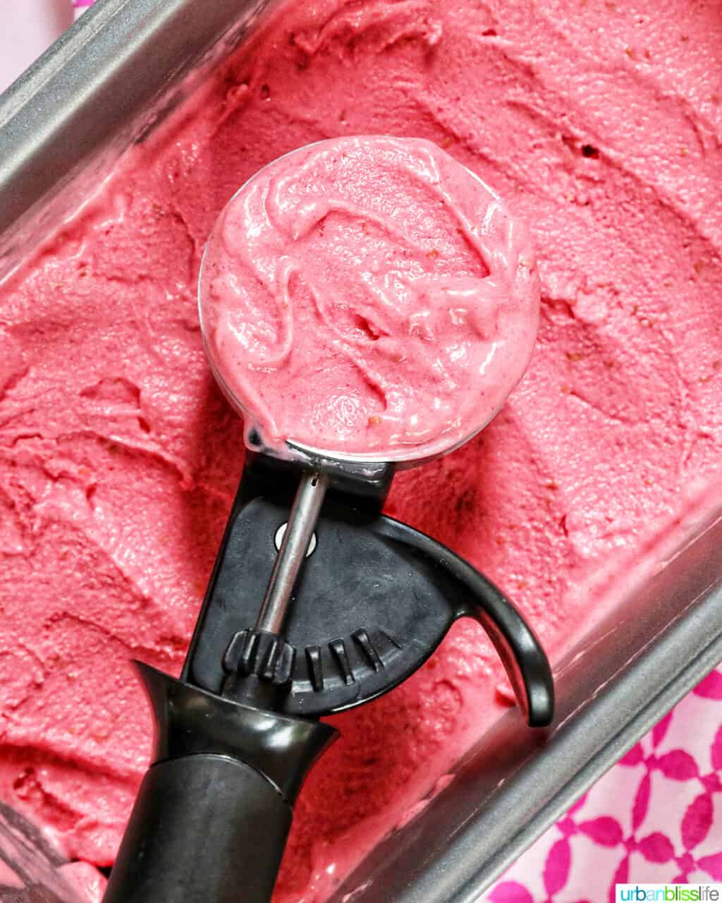 ice cream scoop filled with raspberry sherbet on top of a pan filled with raspberry sherbet.