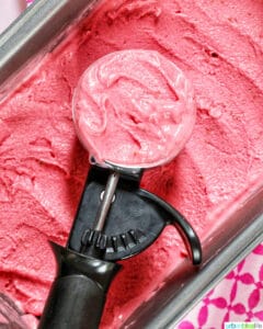 ice cream scoop filled with raspberry sherbet on top of a pan filled with raspberry sherbet.
