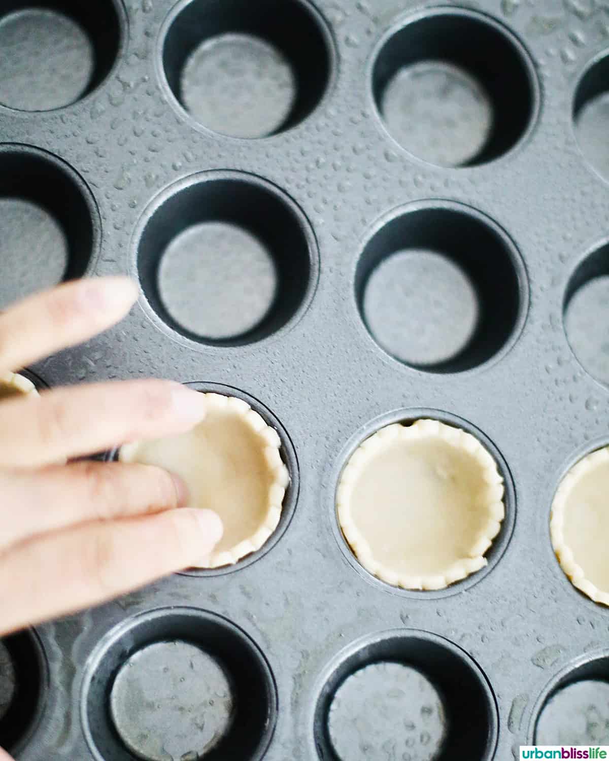 hand pressing pie crust dough into a mini muffin tin.