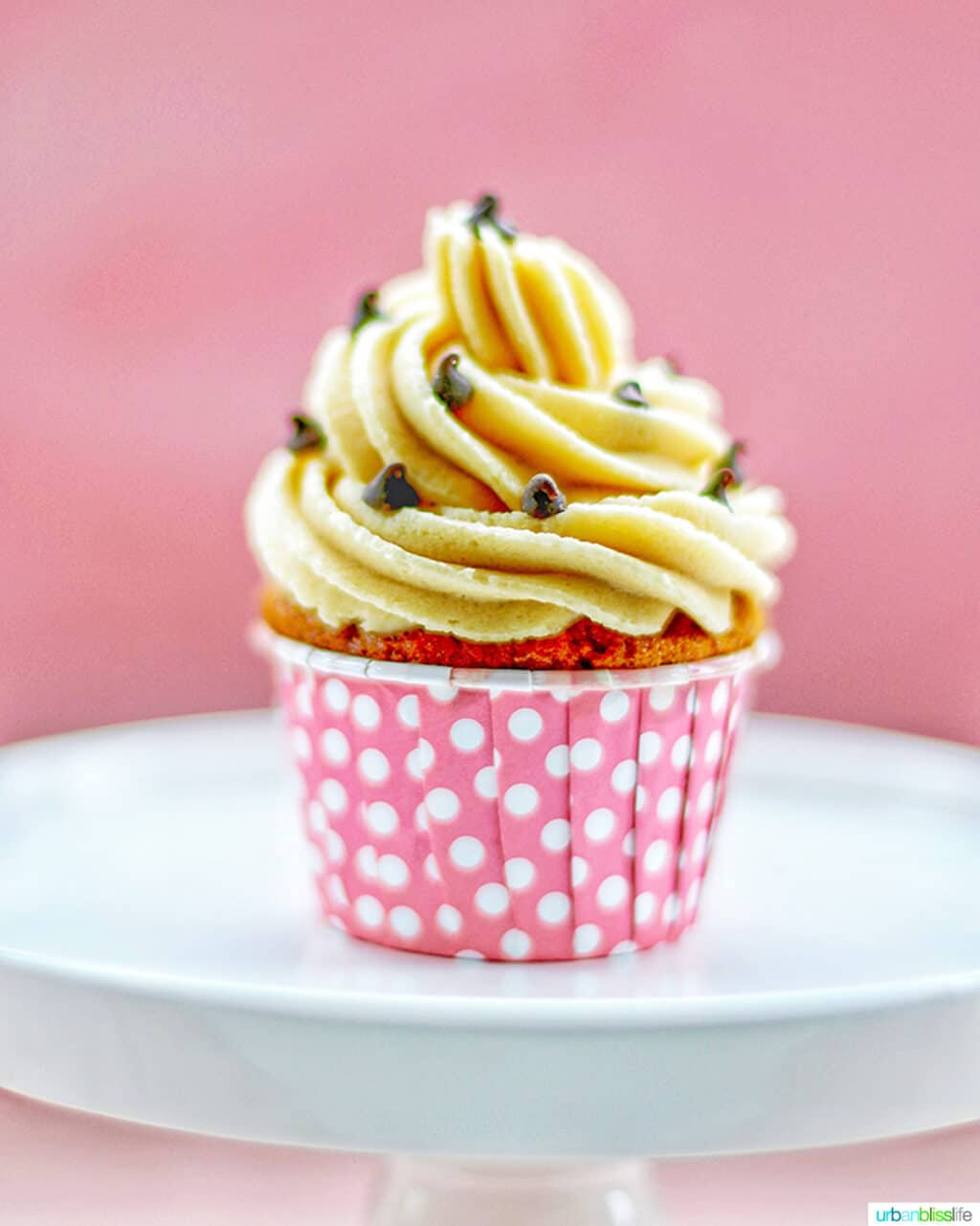 one chocolate chip cupcake with cookie dough frosting in pink cup on white cake pedestal