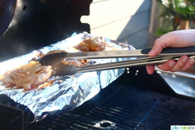 turning over Cider Ginger Grilled Chicken with tongs on the grill.