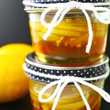 two mason jars of ginger lemon and honey marmalade stacked, with a lemon on the side.