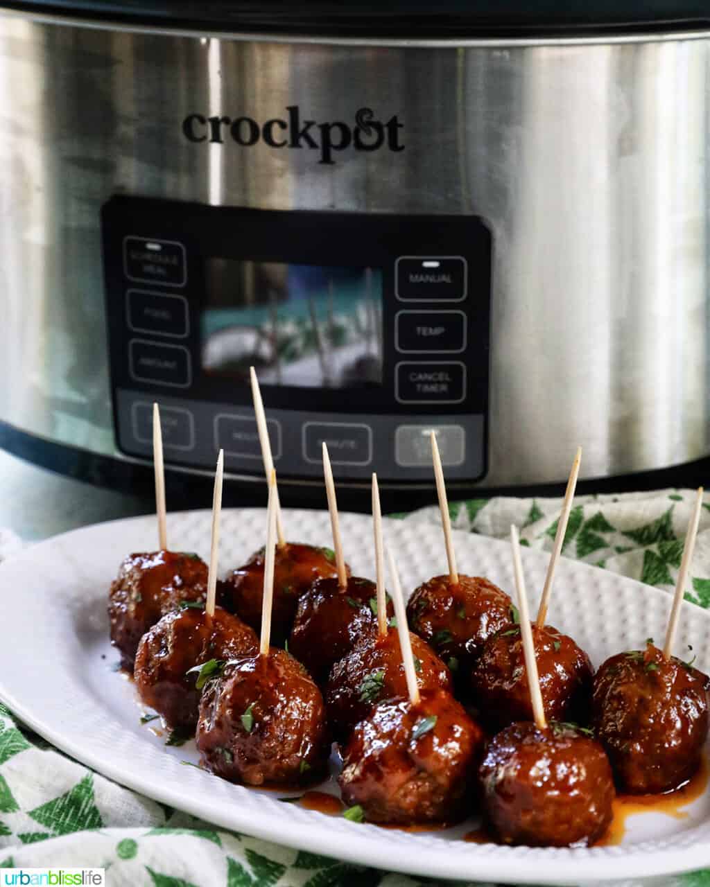 white plate with several honey bourbon meatball appetizers with toothpicks, and a crockpot slow cooker behind the plate.