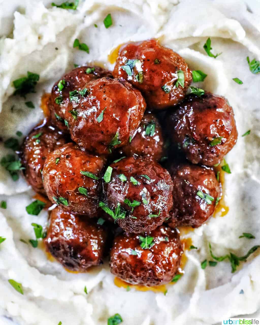 overhead view of several honey bourbon meatballs stacked on top of each other on a bed of mashed potatoes, with chopped parsley garnish.