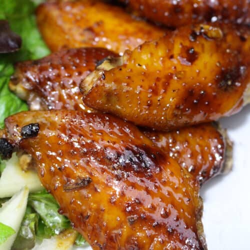 honey bourbon chicken wings stacked next to green salad.