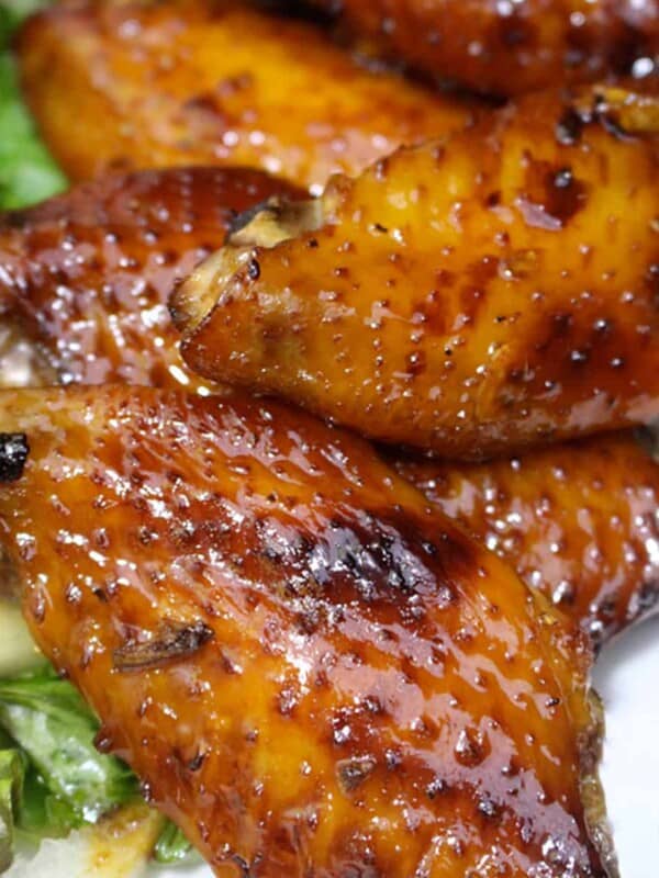 honey bourbon chicken wings stacked next to green salad.