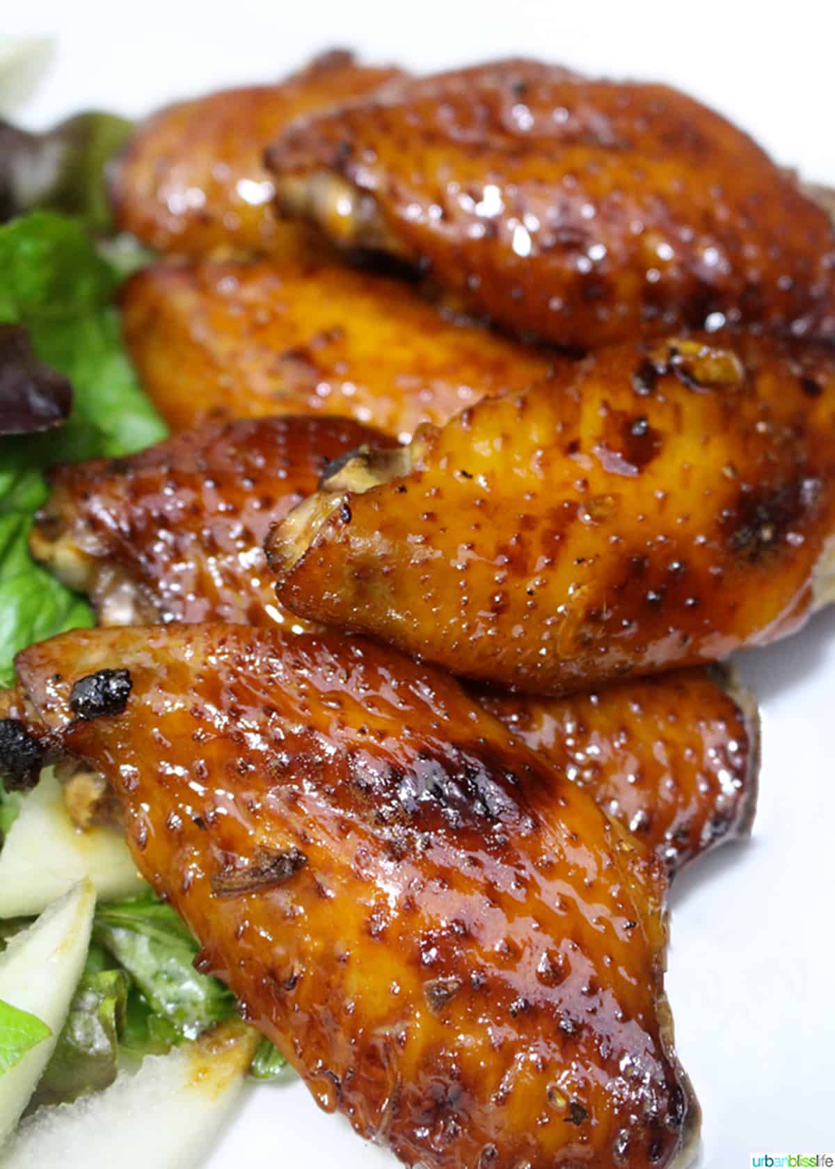 honey bourbon chicken wings stacked on top of each other next to green salad.