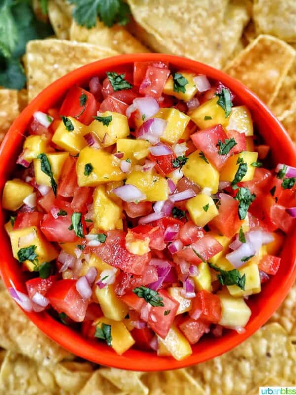 orange bowl filled with mango pico de gallo surrounded by pile of tortilla chips.