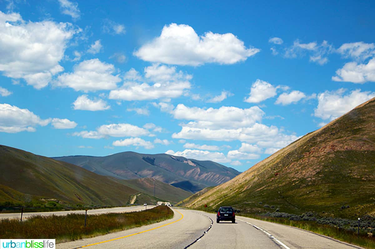 car on a highway with rolling hills and mountains in the background.