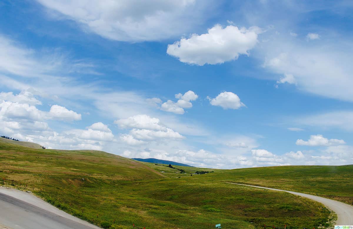 big blue skies with clouds above rolling green hills and a highway.