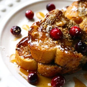 stack of brioche french toast on a white plate with cranberries.