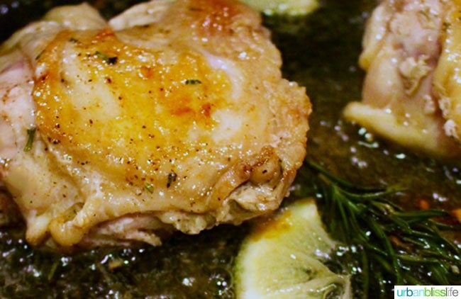 chicken thighs in cast iron skillet with herbs and lemon.