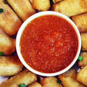 sweet chili dipping sauce in a bowl surrounded by egg rolls.
