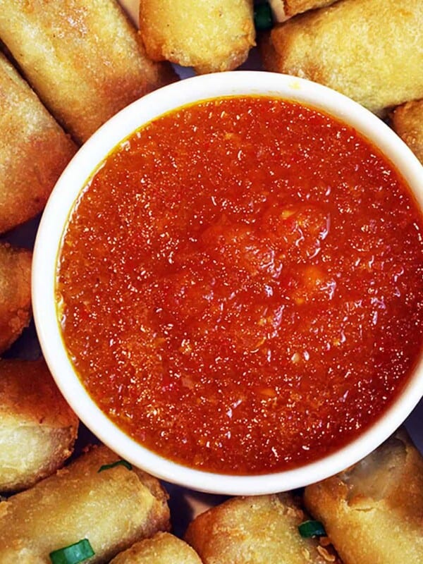 sweet chili dipping sauce in a bowl surrounded by egg rolls.