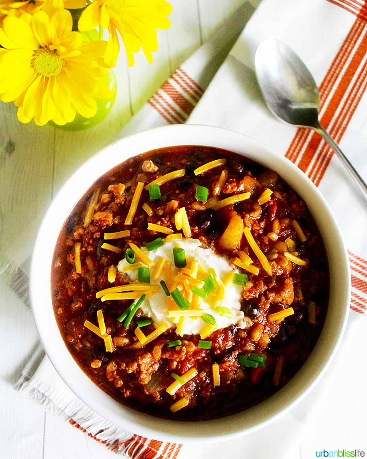 bowl of turkey chili with ground turkey, farro, stout, and toppings with a vase of yellow daisies.