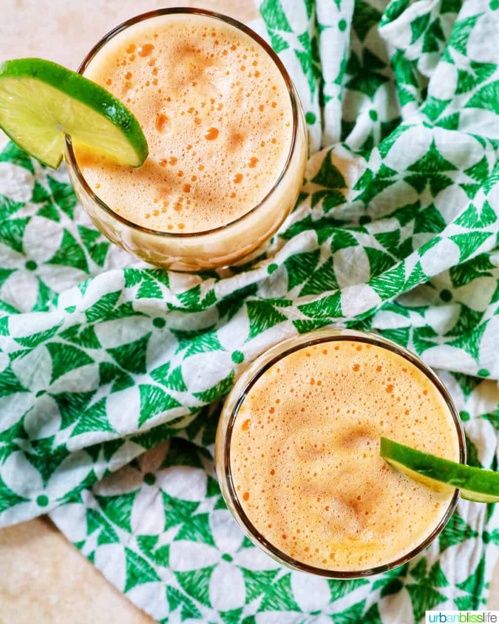 two glasses of cantaloupe margaritas with lime slice garnish on a green and white patterned napkin.