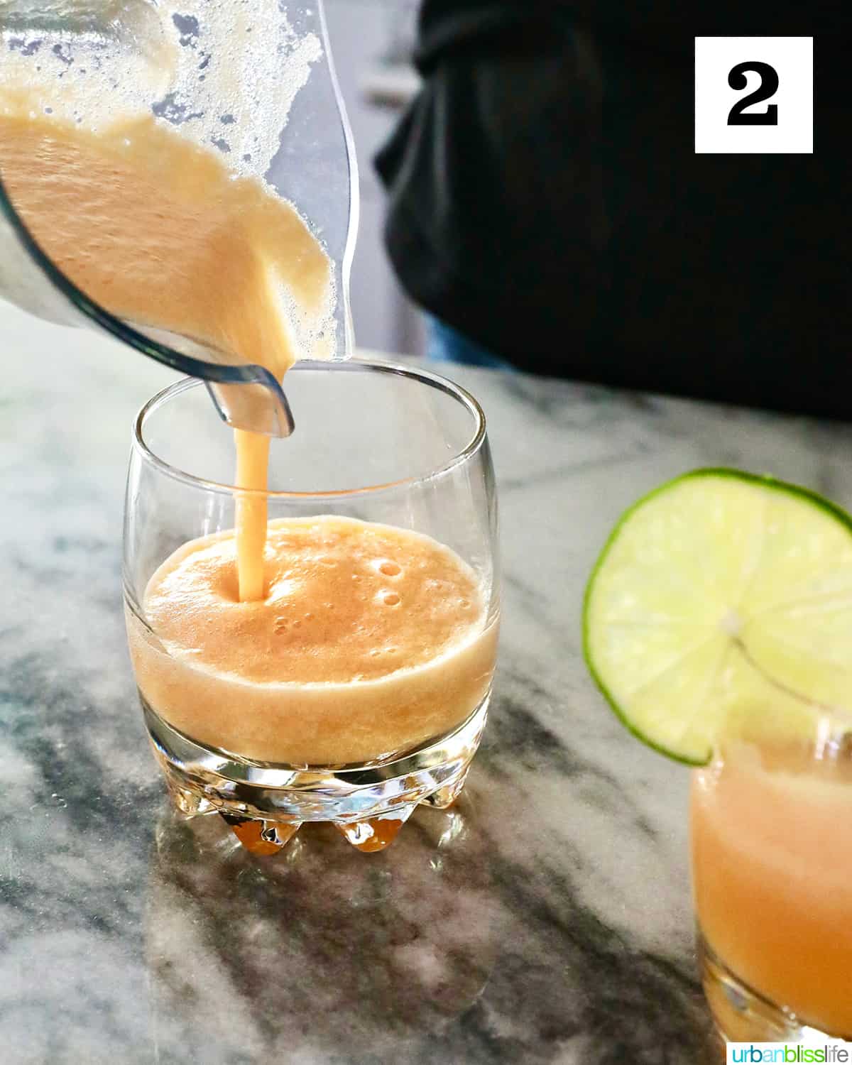 pouring melon margarita from a blender to a glass on a marble countertop.