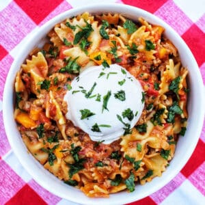 Taco Pasta with scoop of sour cream and chopped parsley on a red and white checkered tablecloth.