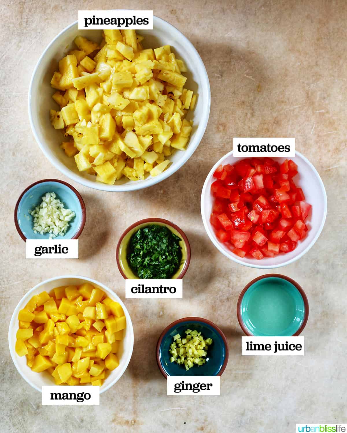 bowls of ingredients to make pineapple mango salsa on a yellow table.