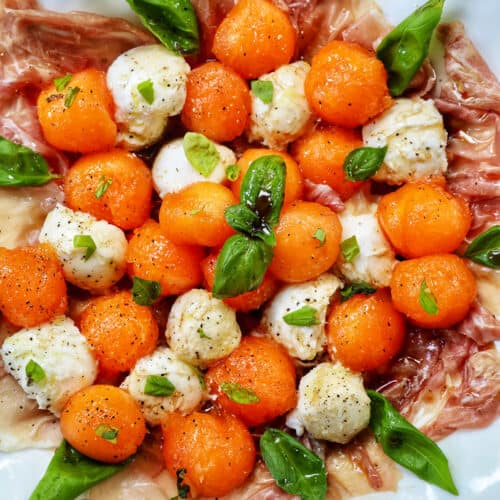 cantaloupe mozzarella prosciutto basil caprese salad on a white plate.