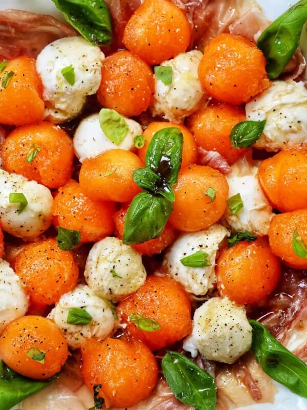 cantaloupe mozzarella prosciutto basil caprese salad on a white plate.