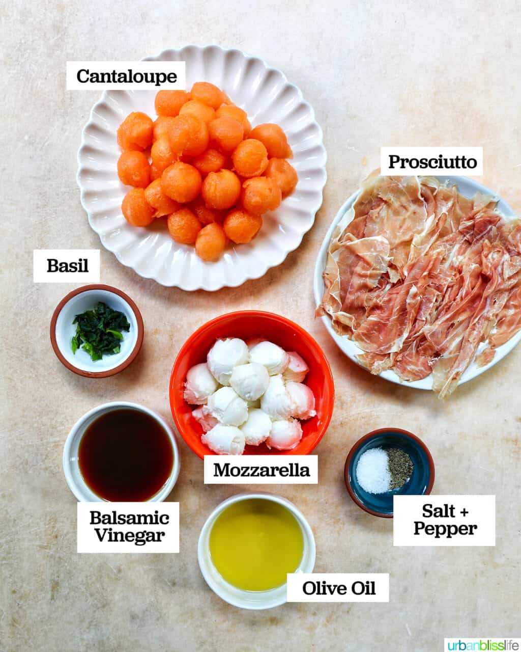 ingredients in bowls and on plates to make melon prosciutto caprese salad on a faded table.