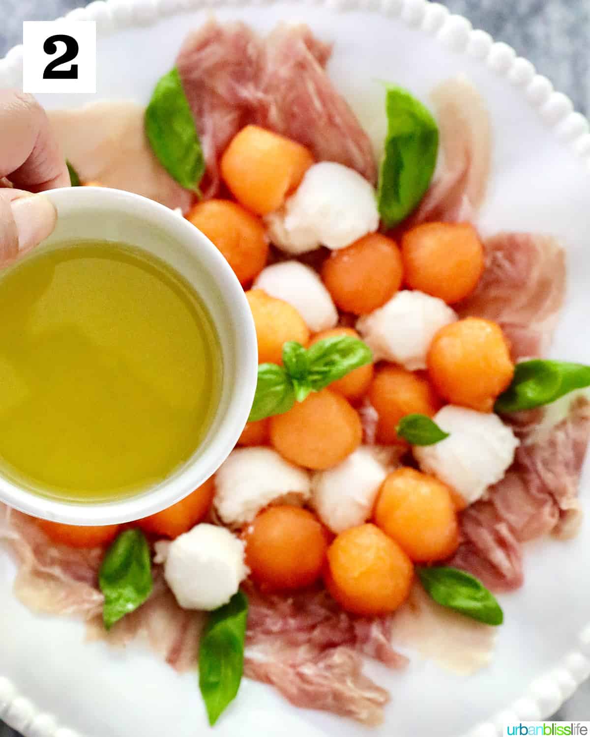 bowl of olive oil to drizzle over melon prosciutto caprese salad on a white bowl.