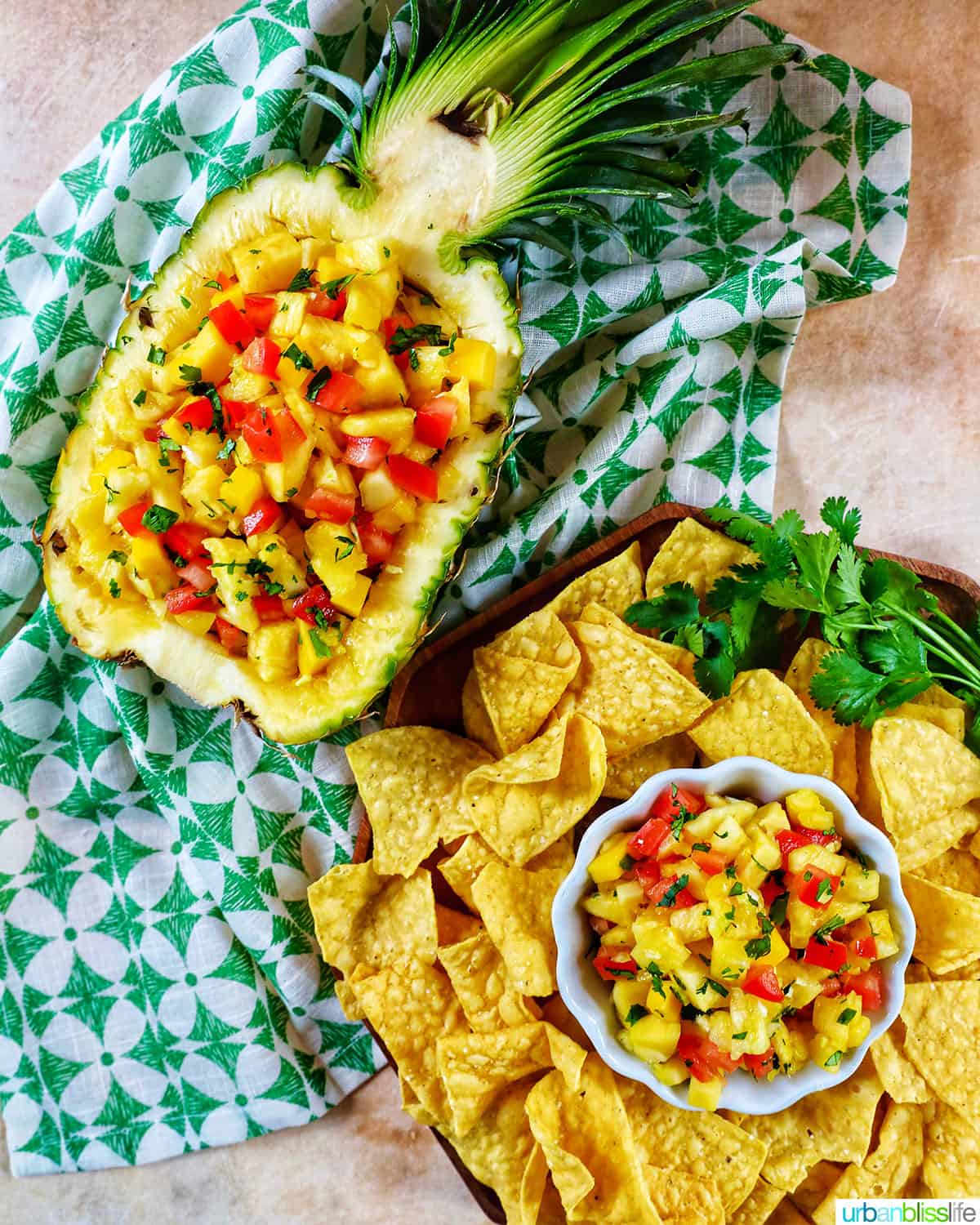 bowl of pineapple mango salsa with tortilla chips and in a hollowed out pineapple on top of a green and white napkin.