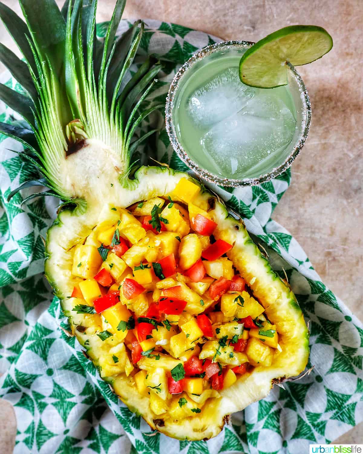 chopped pineapple, mango, tomatoes, and onions in a hollowed out pineapple with glass of margarita.