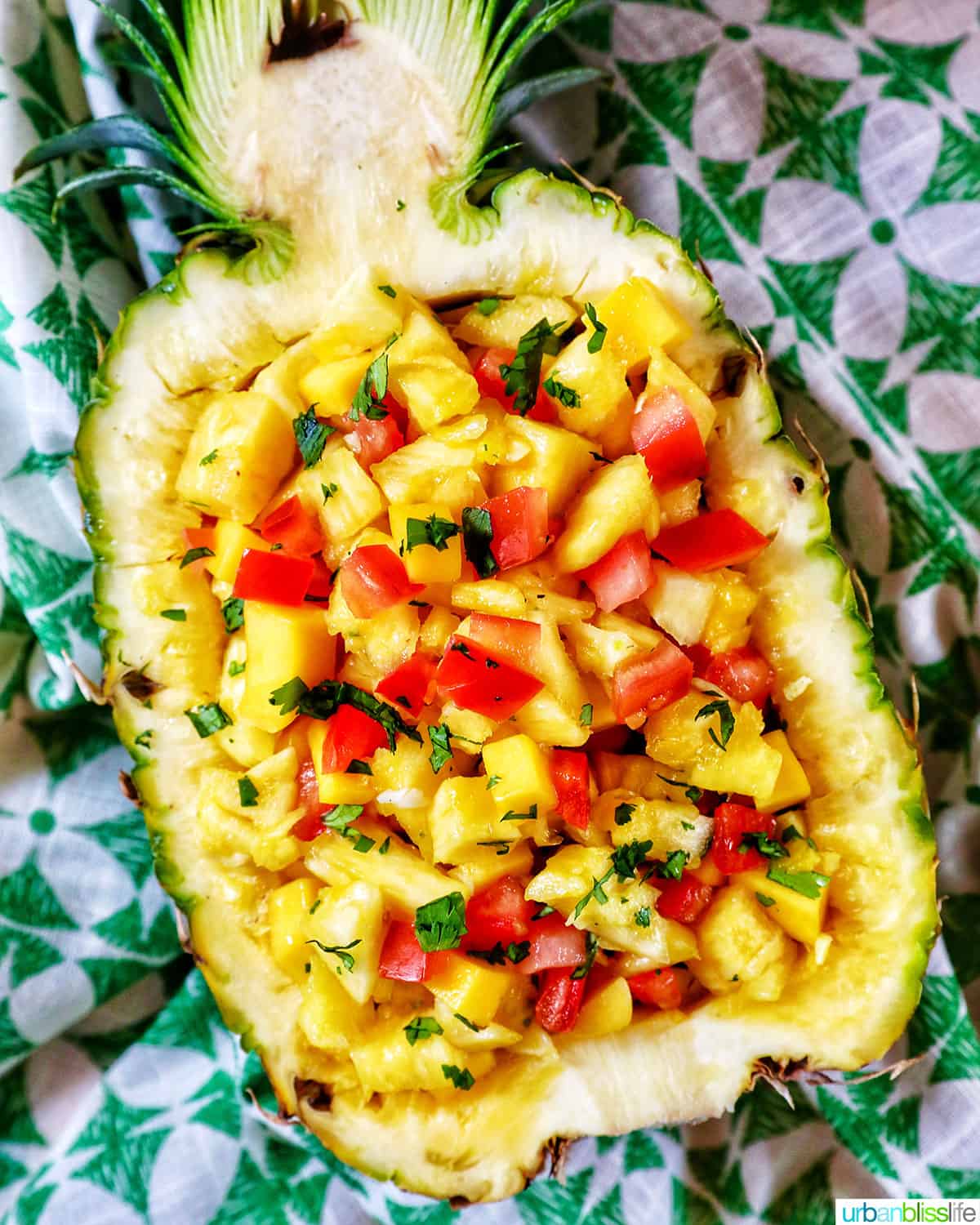 chopped pineapple, mango, tomatoes, and onions in a hollowed out pineapple on green napkin..