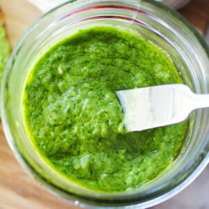 bright green avocado pesto in a mason jar with a small knife placed in the pesto.