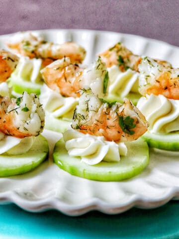 shrimp cucumber cream cheese appetizers on a scalloped plate.