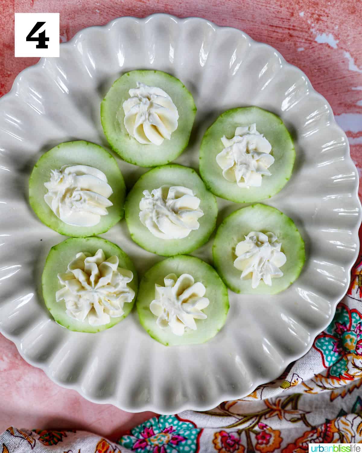 cucumber slices with cream cheese on a scalloped plate on pink background.