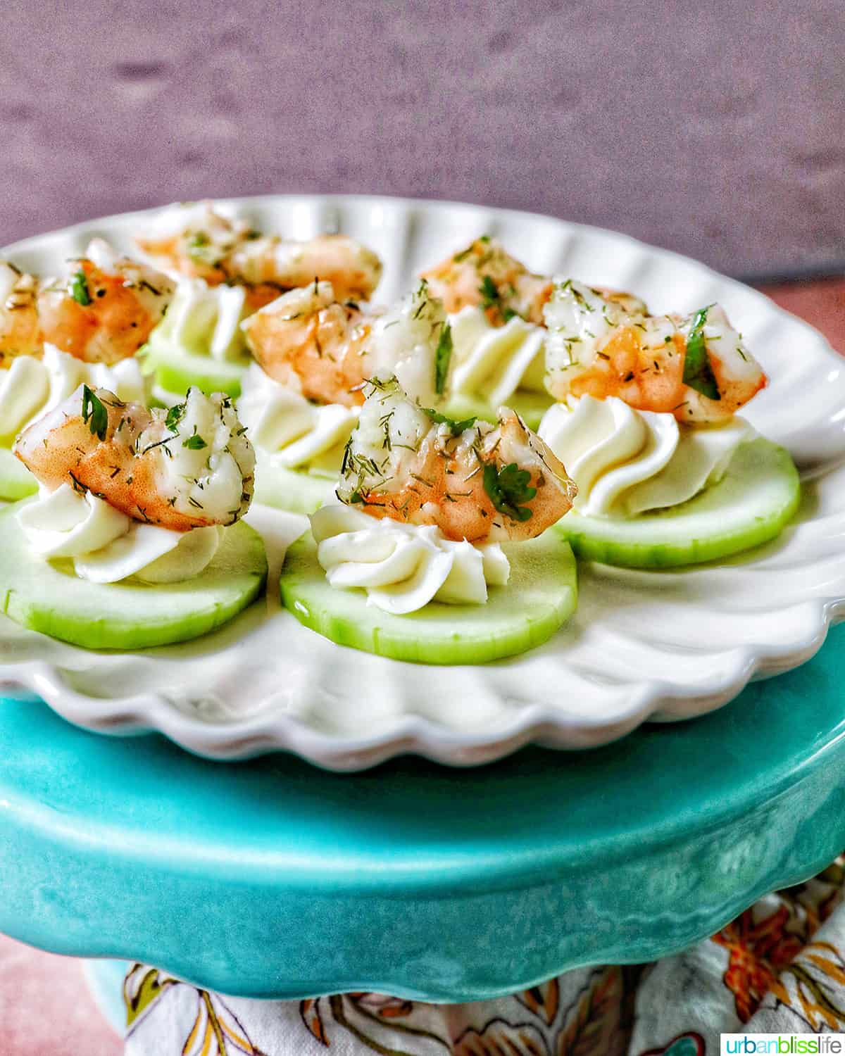 cucumber shrimp canapé appetizers on a white plate on blue pedestal.