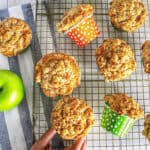 several apple vegetable muffins on a cooling rack with one hand taking a muffin.