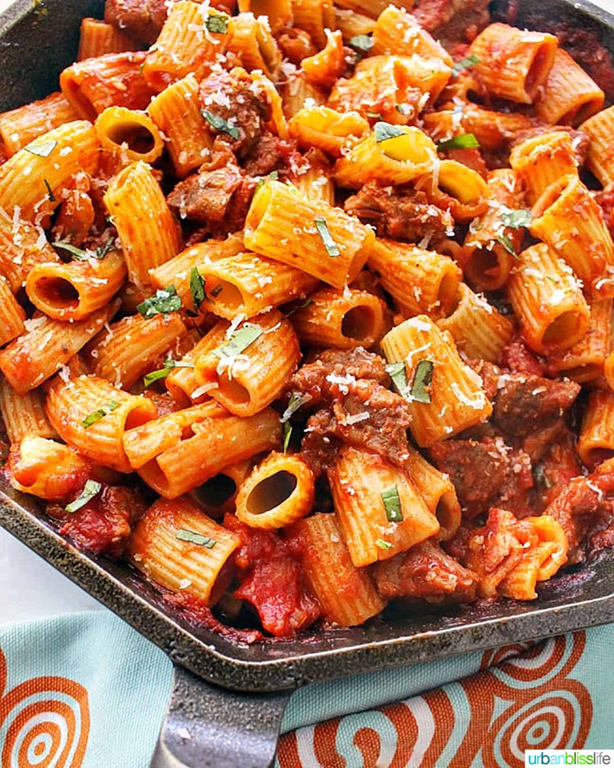 bowl of rigatoni pasta with Italian sausage in a cast iron skillet.