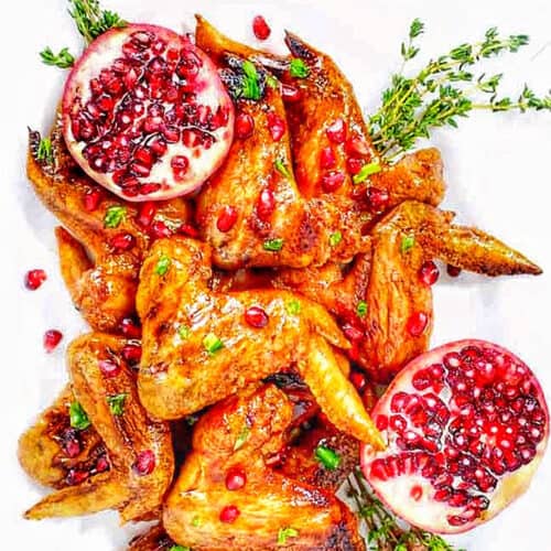 Cranberry Pomegranate Sticky Chicken Wings with herbs and a sliced open pomegranate.