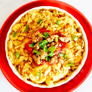 bowl of taco mac and cheese with crushed tortilla chips, tomatoes, and cilantro on an orange plate.