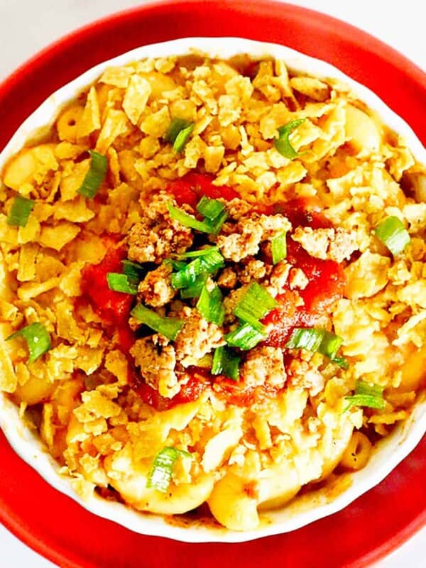 bowl of taco mac and cheese with crushed tortilla chips, tomatoes, and cilantro on an orange plate.