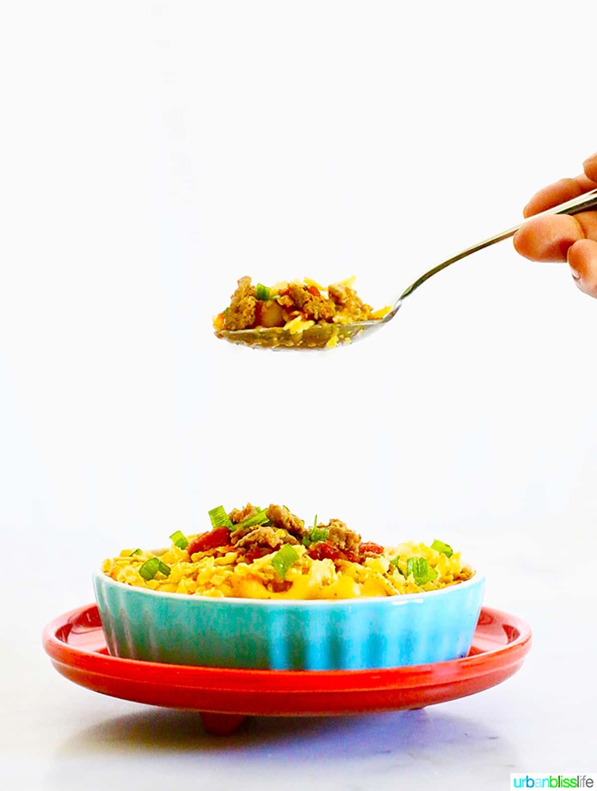 spoon holding some taco mac and cheese above a larger bowl full of taco mac and cheese.