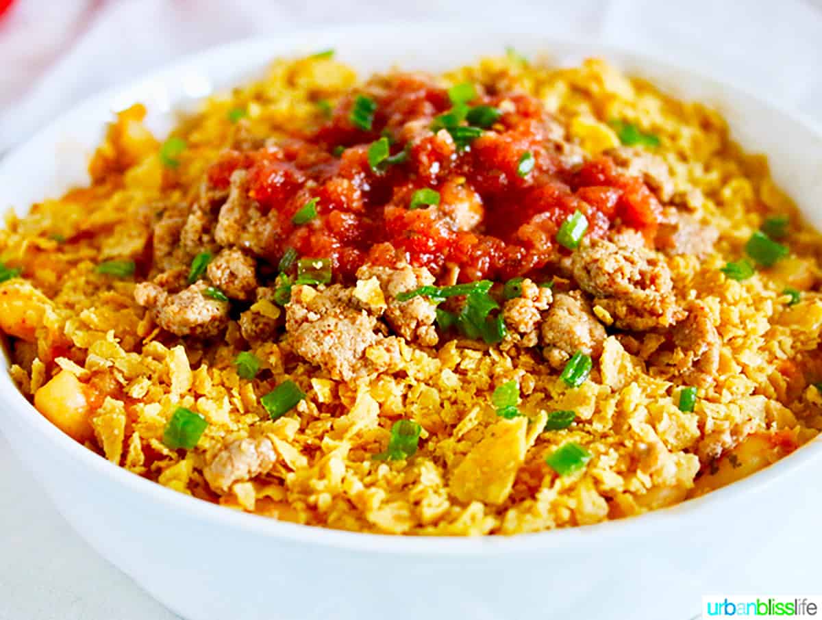 bowl of taco mac and cheese with crushed tortilla chips, tomatoes, and cilantro.