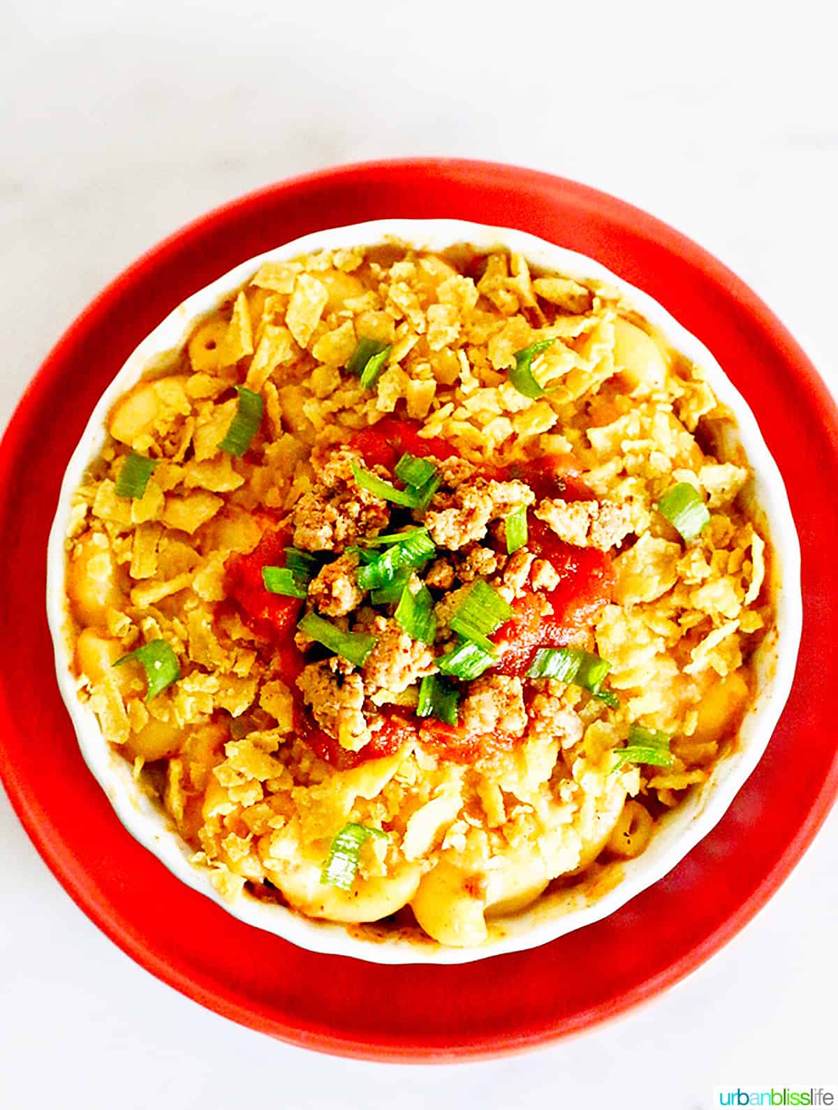 bowl of taco mac and cheese with crushed tortilla chips, tomatoes, and cilantro on an orange plate.