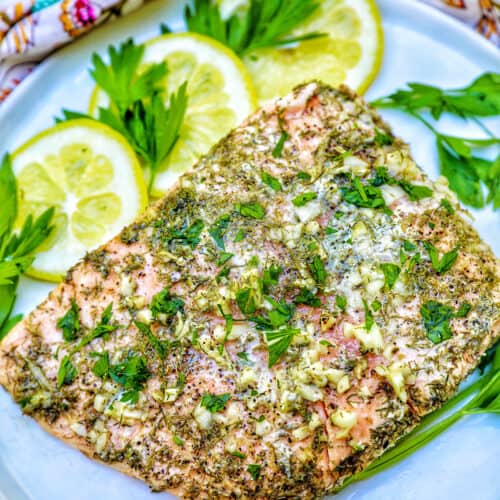 grilled salmon with lemon, garlic, and herbs, with lemon slices on a white plate.