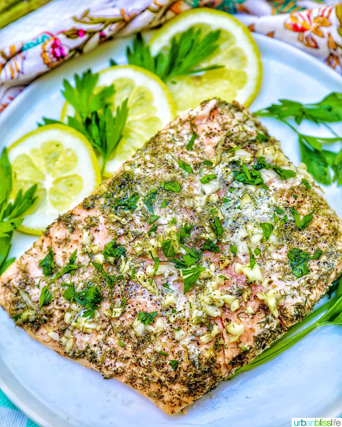 grilled salmon with lemon, garlic, and herbs, with lemon slices on a white plate.
